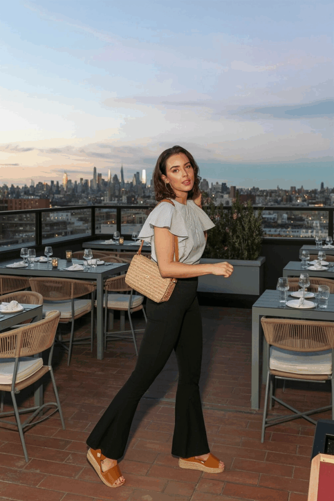 woman mid-step in black flare leggings, a flutter-sleeve cotton blouse, tan espadrille sandals, and a straw crossbody bag