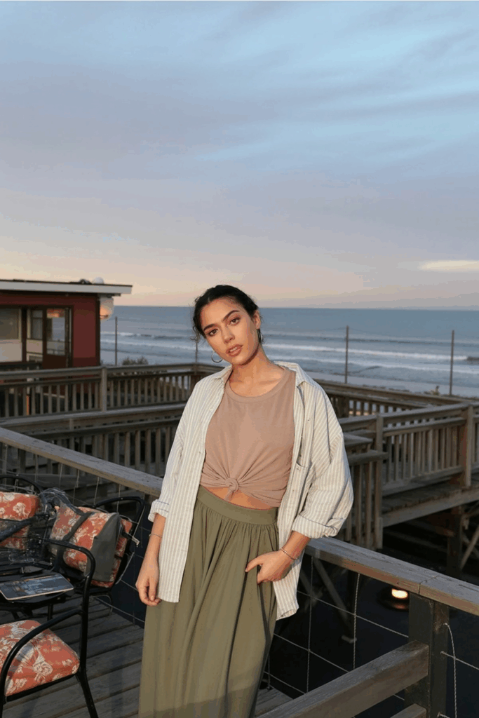 woman wearing a soft olive skirt, tucked beige tee, and an oversized white linen shirt worn open as a light layer