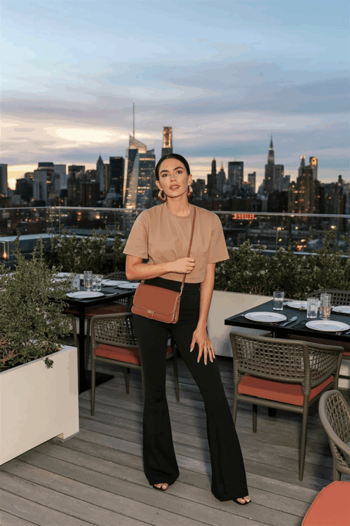 A woman in black flare leggings, a lightweight tan tee, a chestnut leather crossbody bag, gold huggie earrings, and platform sandals. Her nails are neatly polished in nude