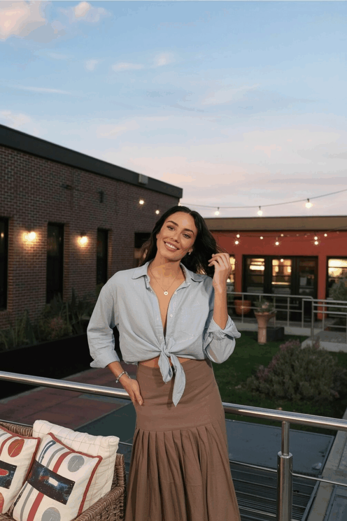 A woman wearing a long, straight-cut mocha skirt with a light gray linen button-down shirt, loosely tucked in.