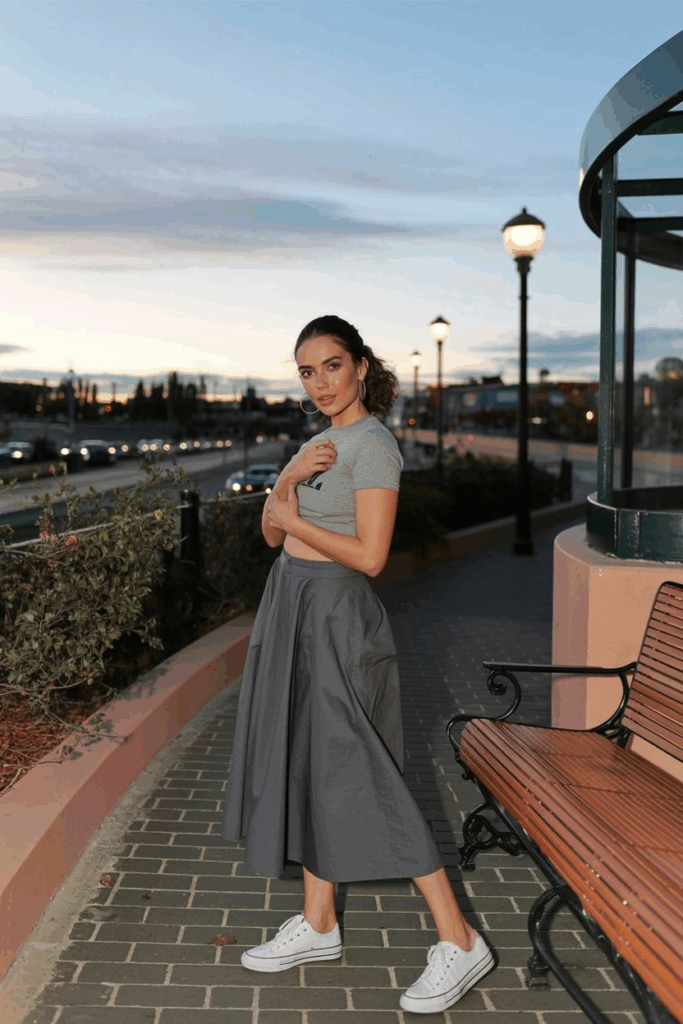 woman wearing a charcoal gray cotton skirt and white canvas sneakers, styled with a tucked-in tee