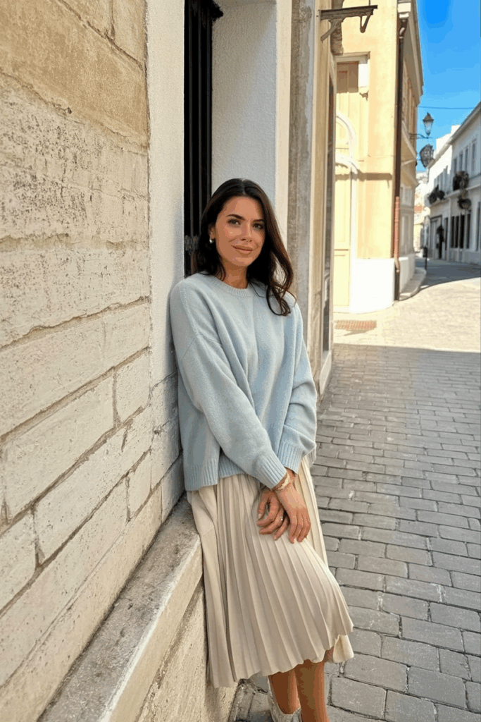 woman draping a soft pastel cashmere sweater over her shoulders, styled over a midi dress