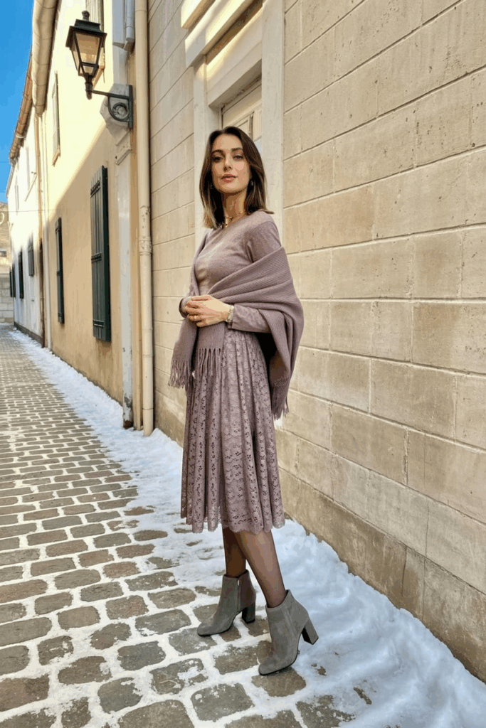 A woman wearing a dusty mauve lace midi dress with long sleeves, thick thermal tights, a matching wool shawl, and gray suede heeled boots