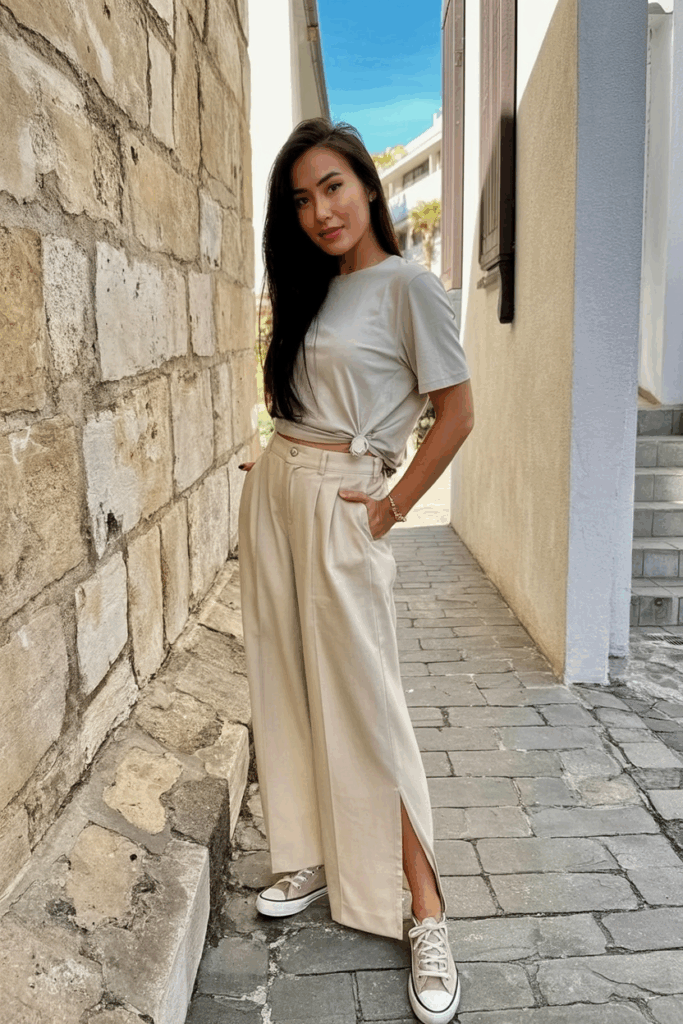 woman wearing a soft beige wide-leg cropped trousers with side slits, paired with a tucked-in minimalist tee and canvas sneakers