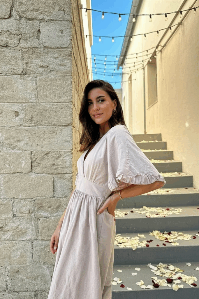 Woman wearing a blush-toned linen dress with flutter sleeves.