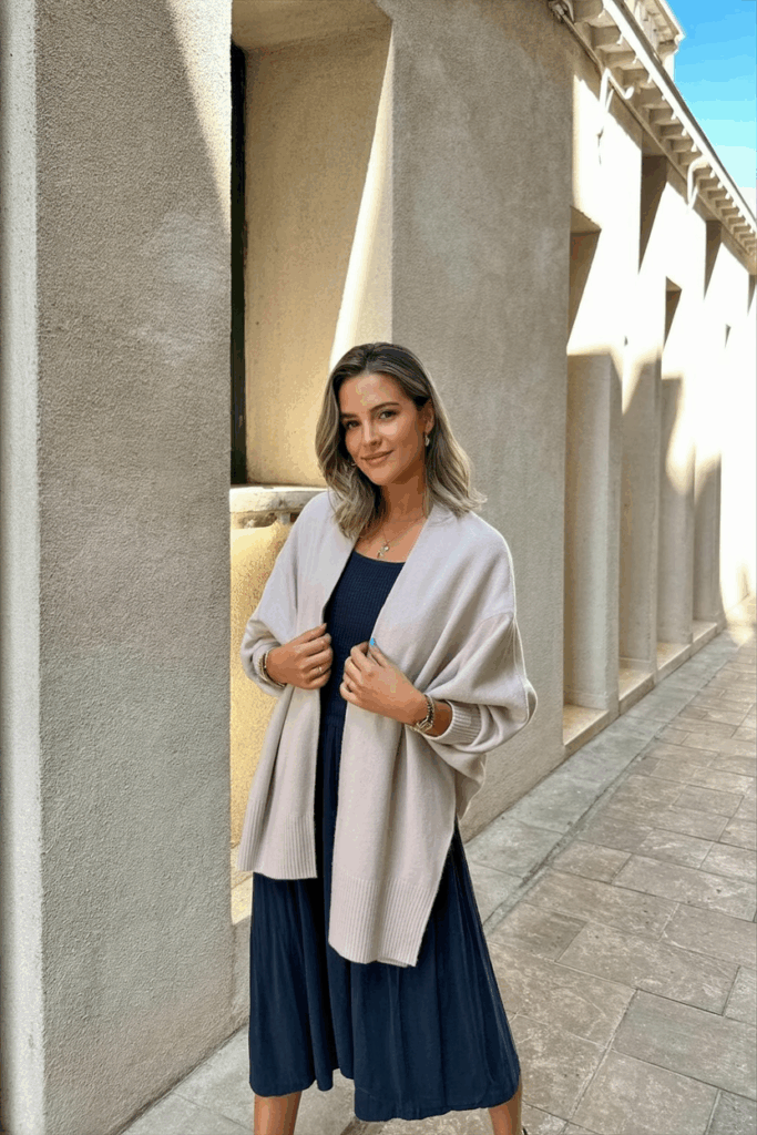 woman draping a soft pastel cashmere sweater over her shoulders, styled over a midi dress