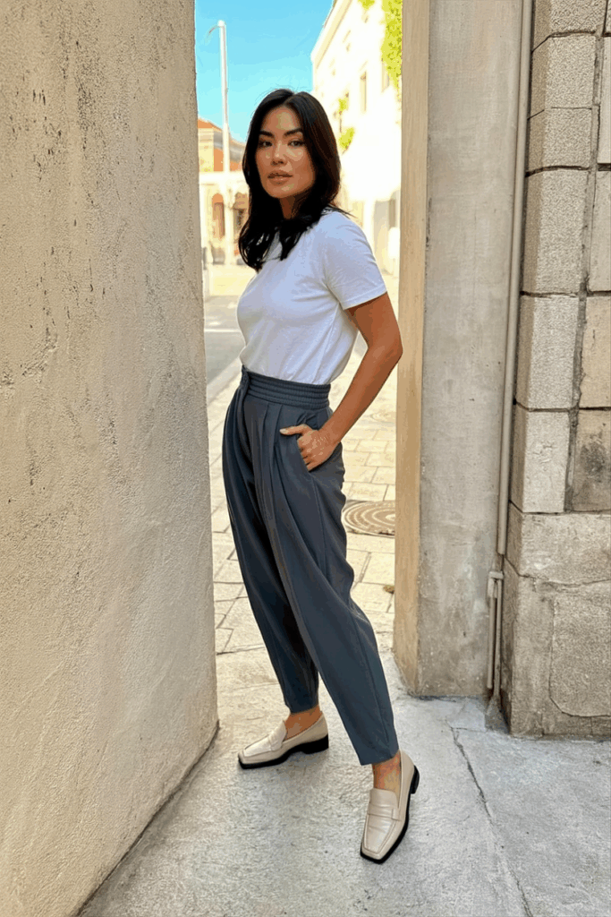 woman wearing charcoal gray tailored joggers with a defined waistband and subtle pleats paired with a clean white tee and loafers