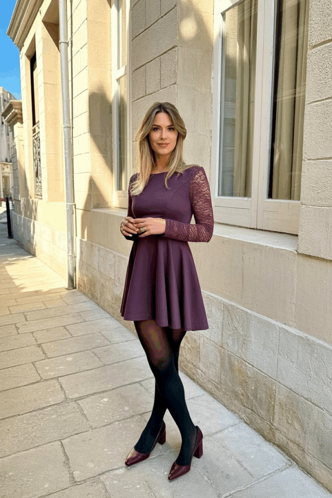 A woman wearing a plum fit-and-flare dress with lace long sleeves, black fleece-lined tights, and burgundy block-heeled pumps