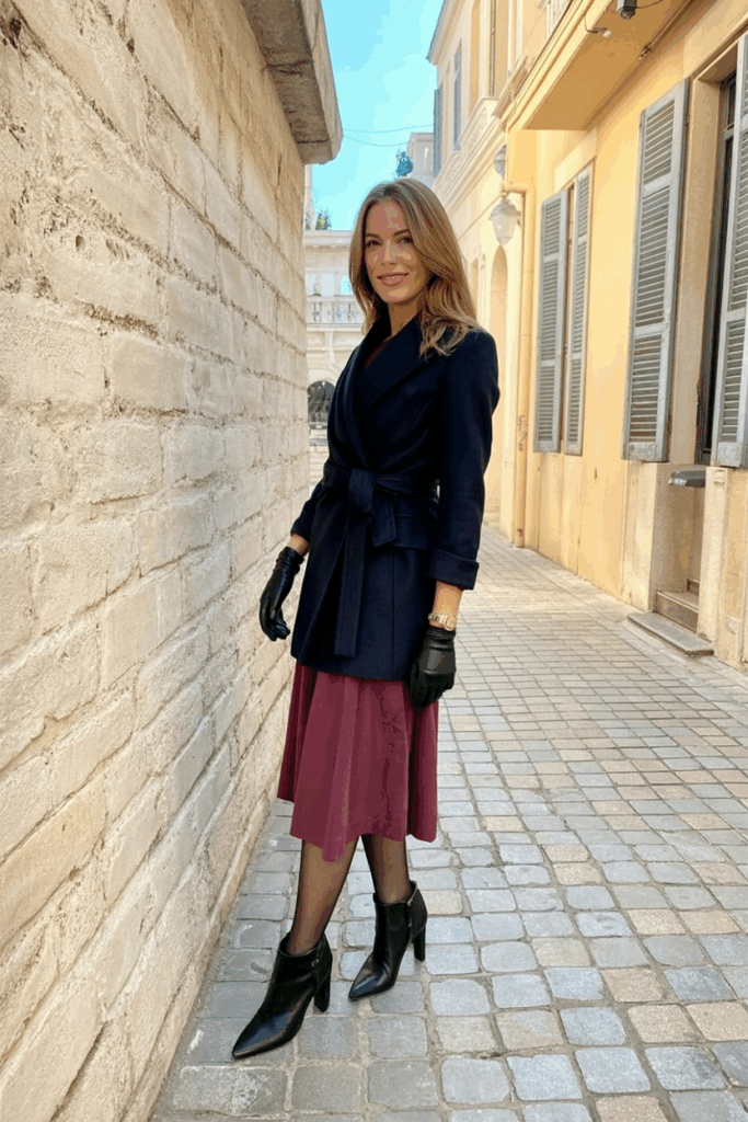 woman wearing a tailored navy wool wrap coat over a burgundy midi dress, black opaque tights, leather gloves, and black heeled booties