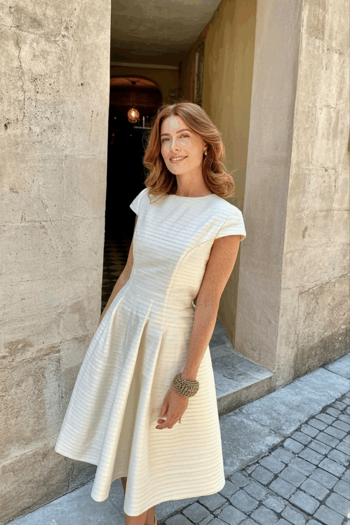 A woman in a beautifully tailored cap sleeved A-line ivory dress.