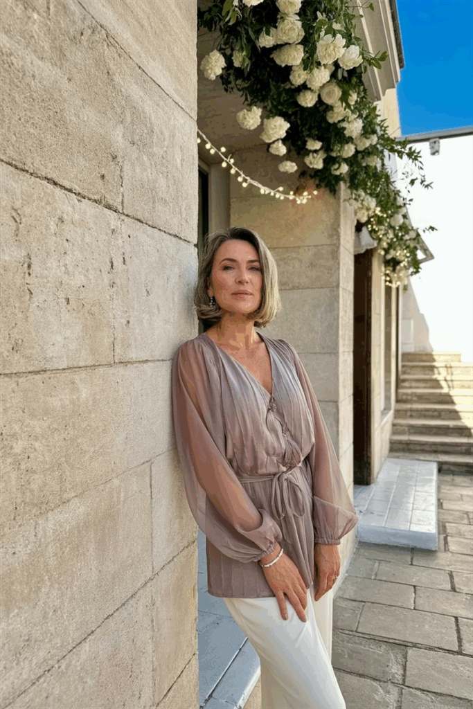 A woman in her 50s wearing wearing an elegant chiffon dress with Sheer long sleeve in muted rose