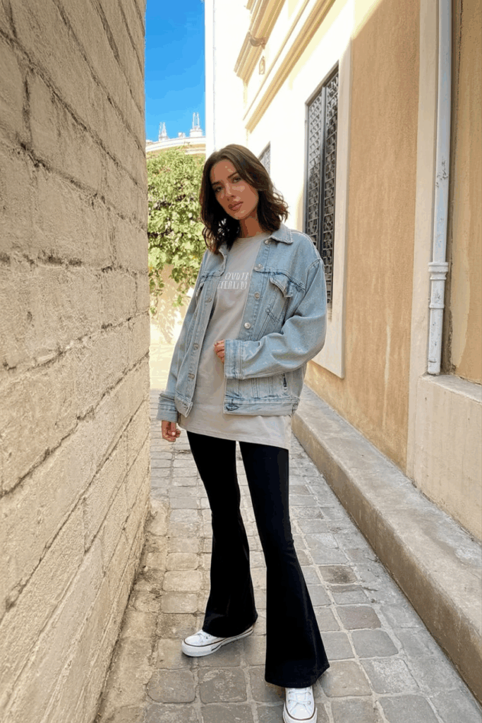 A woman styled in black flare leggings, an oversized light-gray tee, a light-wash denim jacket
