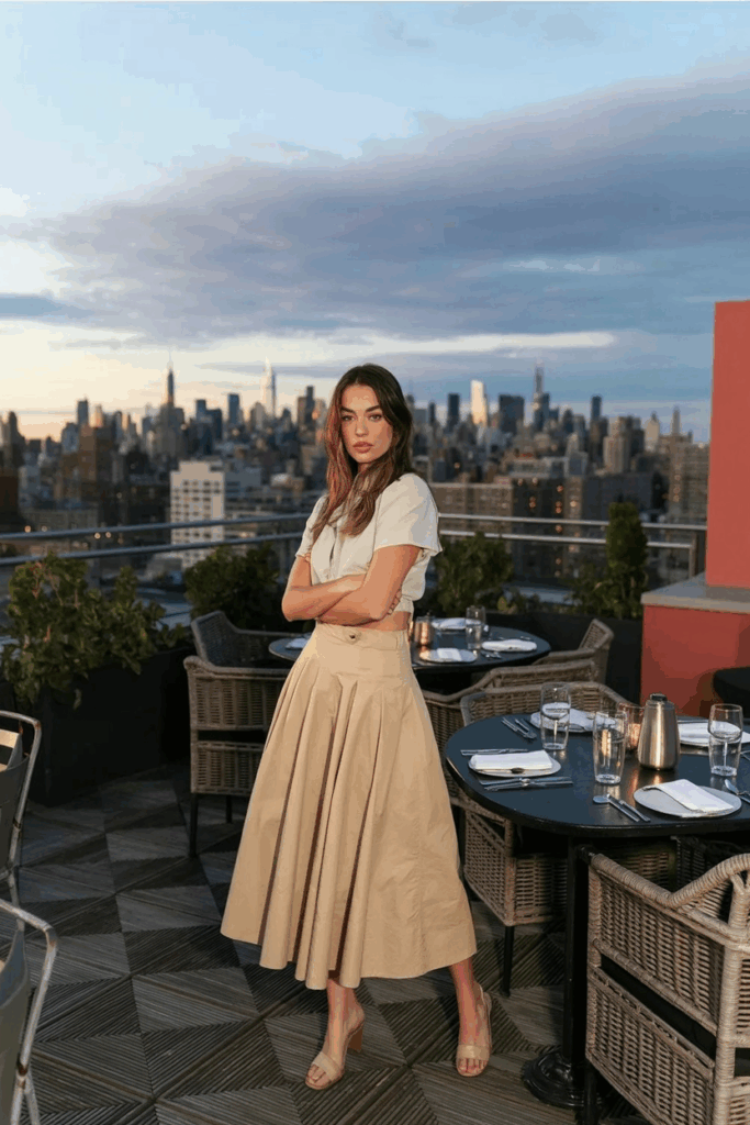 A woman wearing a high-waisted beige A-line cotton skirt that falls to the ankles, paired with a tucked-in cream blouse
