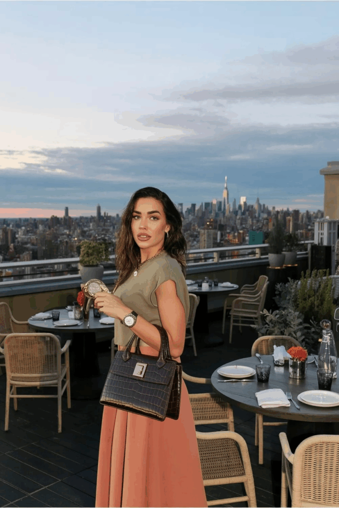 woman holding a structured vintage-style leather handbag, wearing soft earth tones and gold accessories
