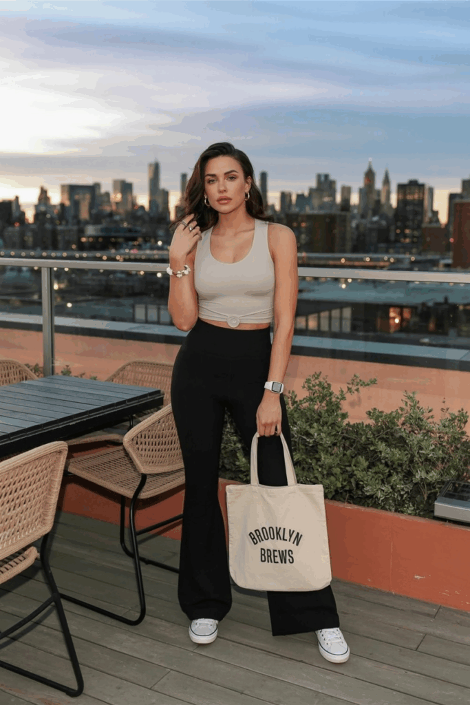 woman pale looking woman in sleek, high-waisted black flare leggings, a tucked-in ivory seamless tank top, white low-top sneakers, and small gold hoops
