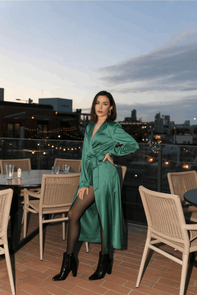 woman wearing a luxurious long-sleeved emerald green maxi wrap dress with a matching belt, black opaque tights, and heeled black ankle boots