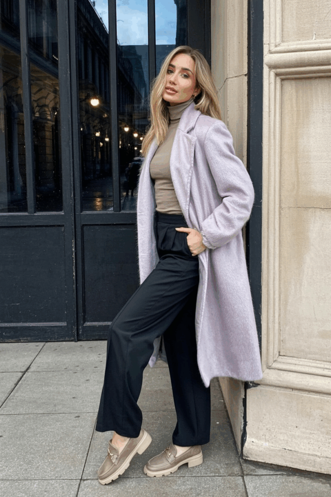 woman wearing a soft mohair-blend coat in pale lilac, styled over a neutral turtleneck and flowy trousers. She adds taupe loafers and a pale scarf to soften the outfit