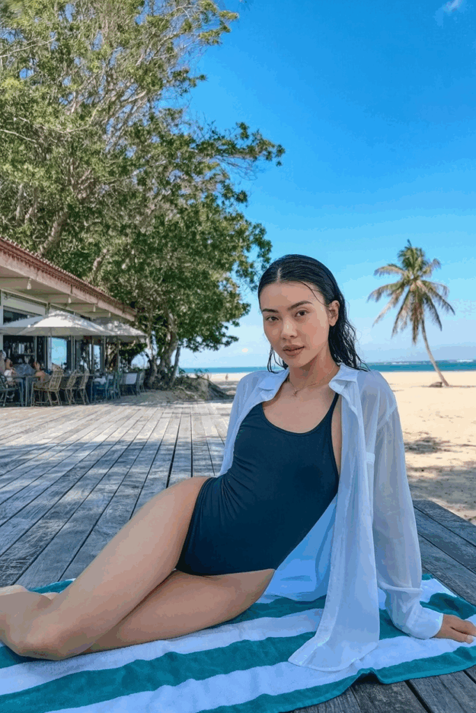 sleek black one-piece swimsuit under a long, unbuttoned sheer white shirt