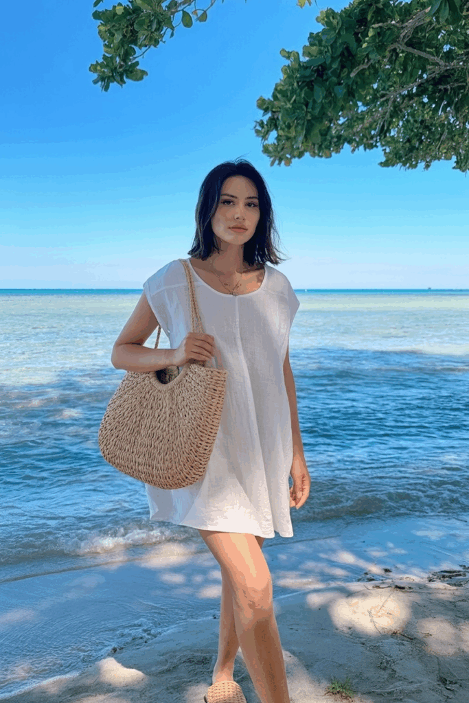 loose white dress with a structured straw tote over one shoulder, flat raffia slides,