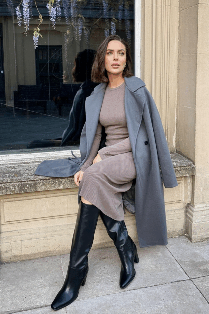 A woman wearing a soft gray cashmere wrap coat over a taupe knit midi dress and black knee-high boots