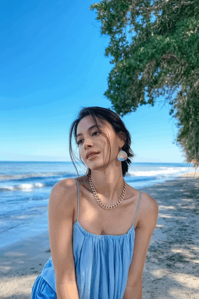 Close-up of a woman's neck and ears, showing delicate gold chain necklace and small shell earrings