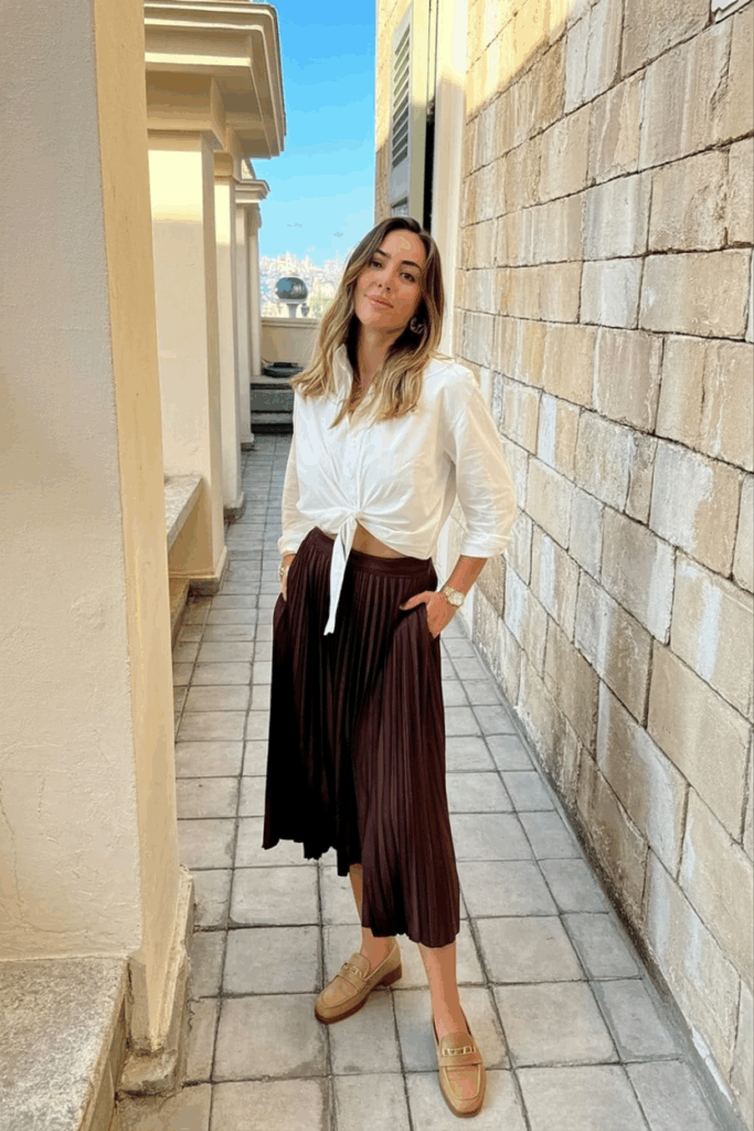 woman wearing a white blouse tucked into a brown pleated skirt with tan loafers