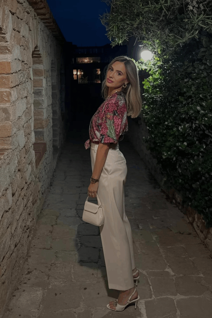 a printed blouse tucked into beige wide-leg trousers with kitten heels and a small top-handle bag