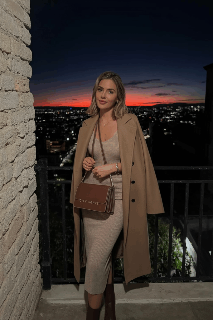 woman wearing a camel wool coat over a fitted knit midi dress, tall brown boots, and a leather shoulder bag