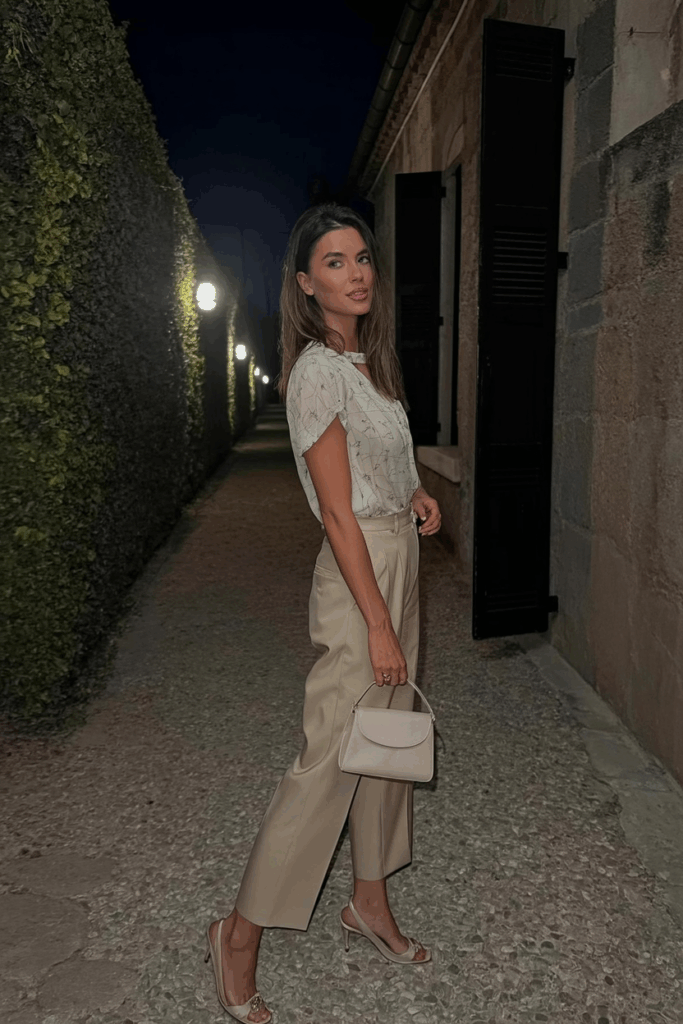 a printed blouse tucked into beige wide-leg trousers with kitten heels and a small top-handle bag