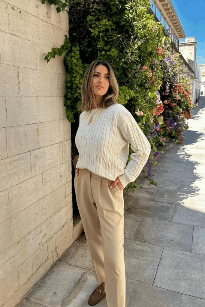 woman wearing a cream cable-knit cashmere sweater tucked into beige high-waisted trousers with brown loafer