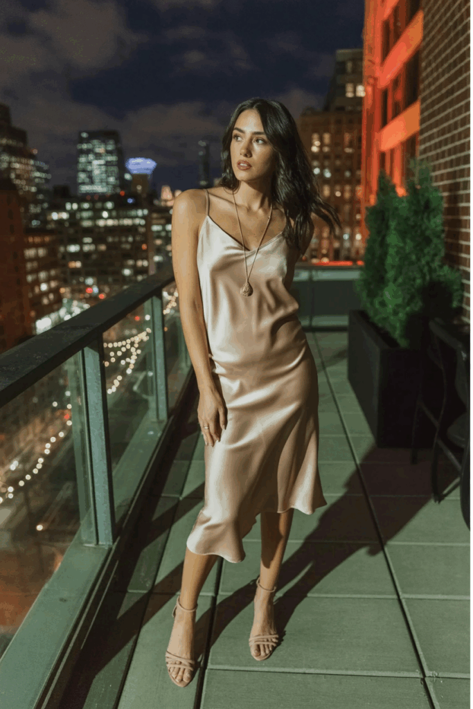 champagne satin slip dress with delicate spaghetti straps, nude strappy heels, and a dainty gold pendant necklace