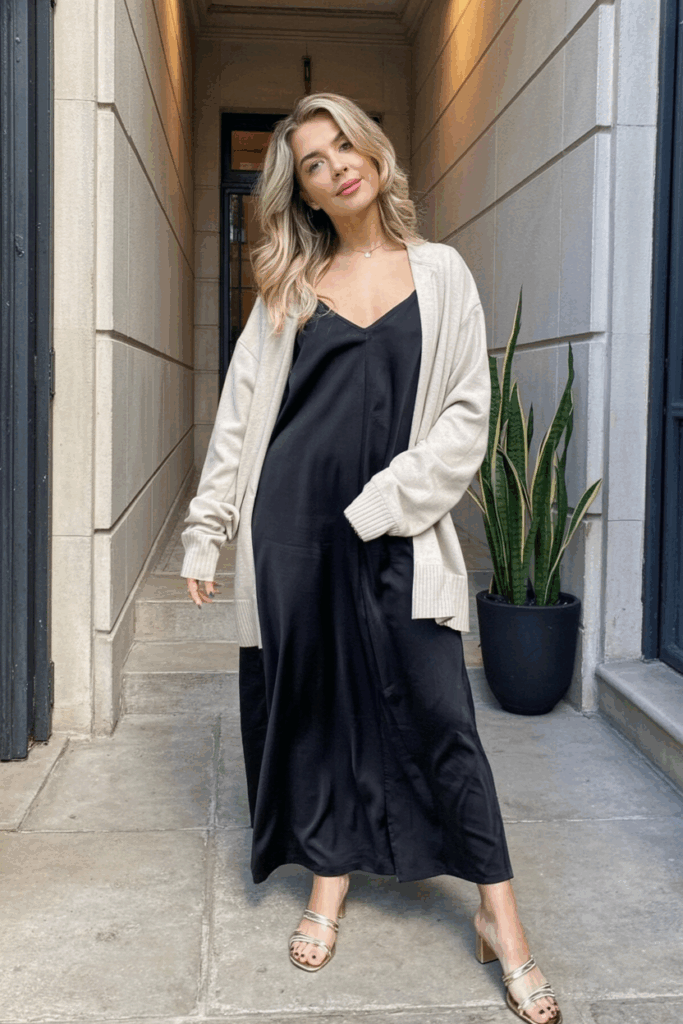 A woman wearing a beige slip dress layered with a white cardigan and strappy sandals