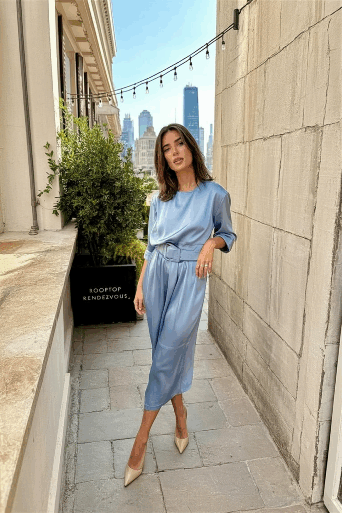 A woman wearing a blue powder silk midi dress with a structured waist and nude kitten heels
