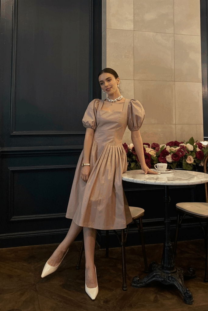 blush tea-length dress with puff sleeves, white low heels, and pearl studs