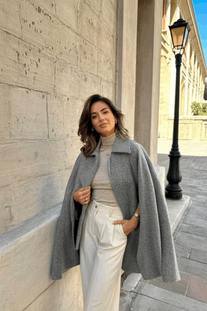 A woman wearing a gray tweed cape with a wool turtleneck and slacks