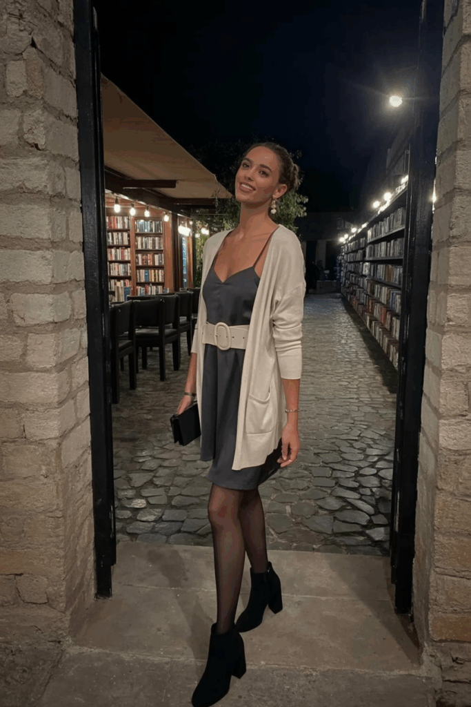 cream belted cardigan over a charcoal slip dress, black tights, and block-heeled ankle boots