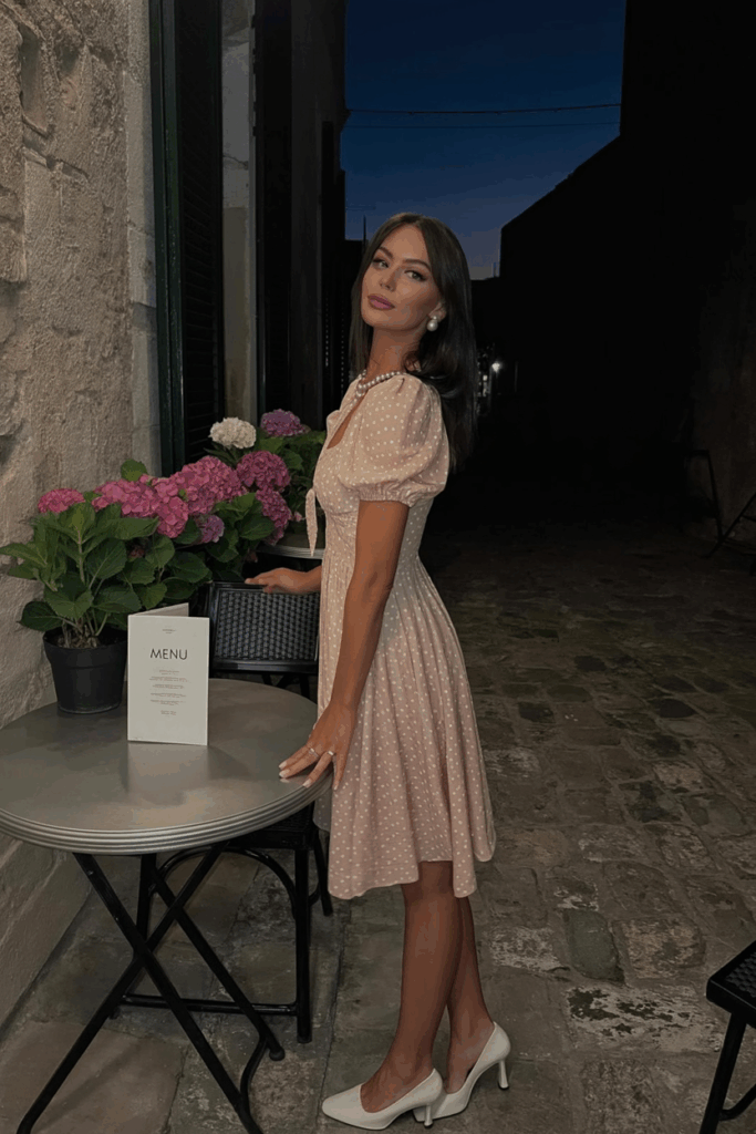 blush tea-length dress with puff sleeves, white low heels, and pearl studs