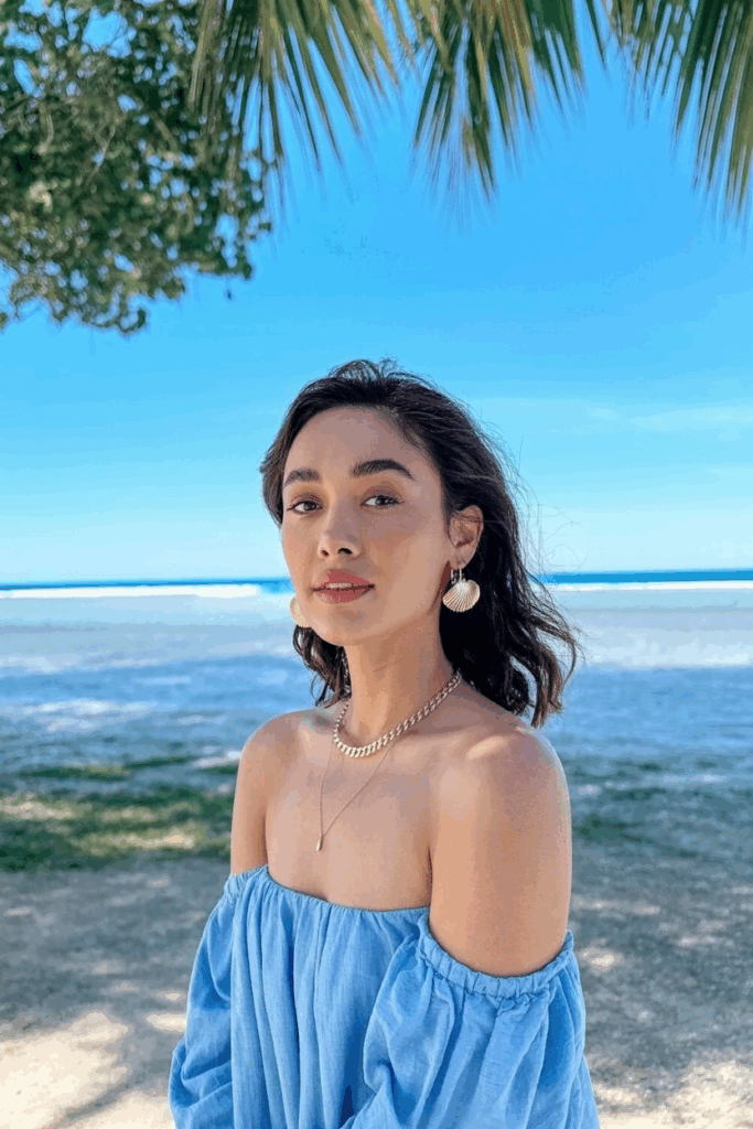 Close-up of a woman's neck and ears, showing delicate gold chain necklace and small shell earrings