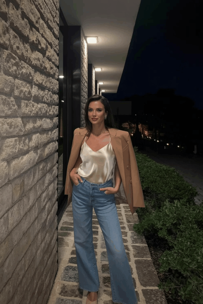 light blue wide-leg jeans, a cream silk camisole, a tan blazer draped over her shoulders, and nude heels