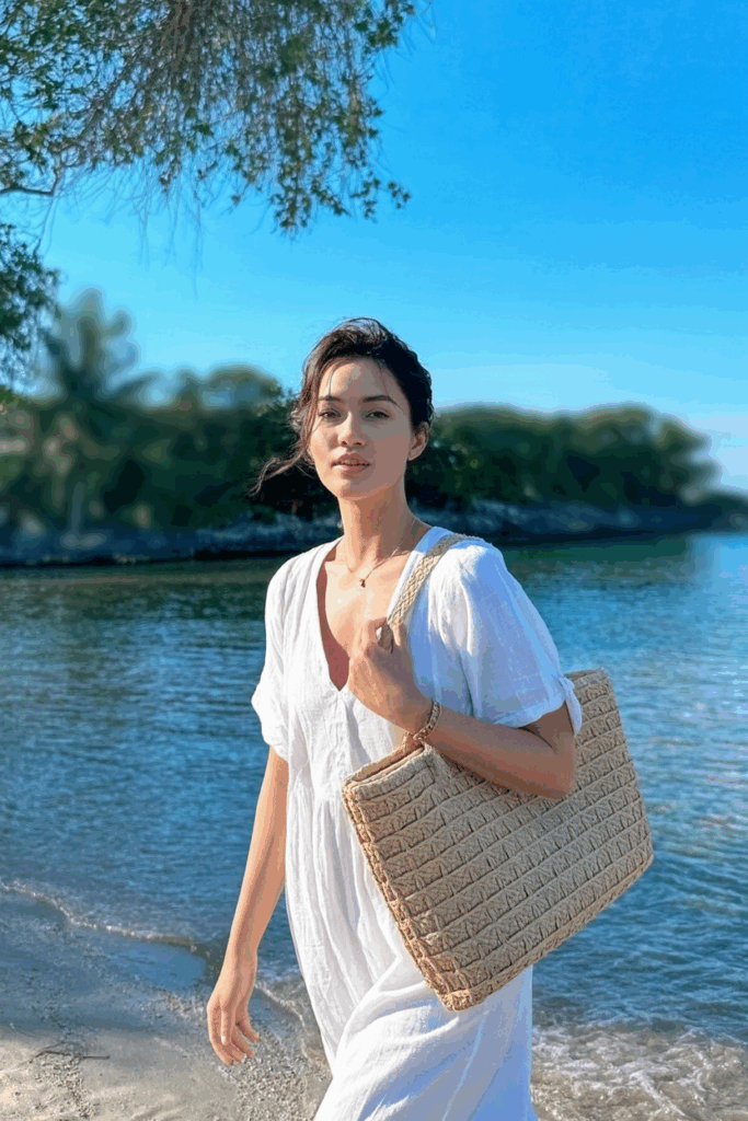 loose white dress with a structured straw tote over one shoulder, flat raffia slides