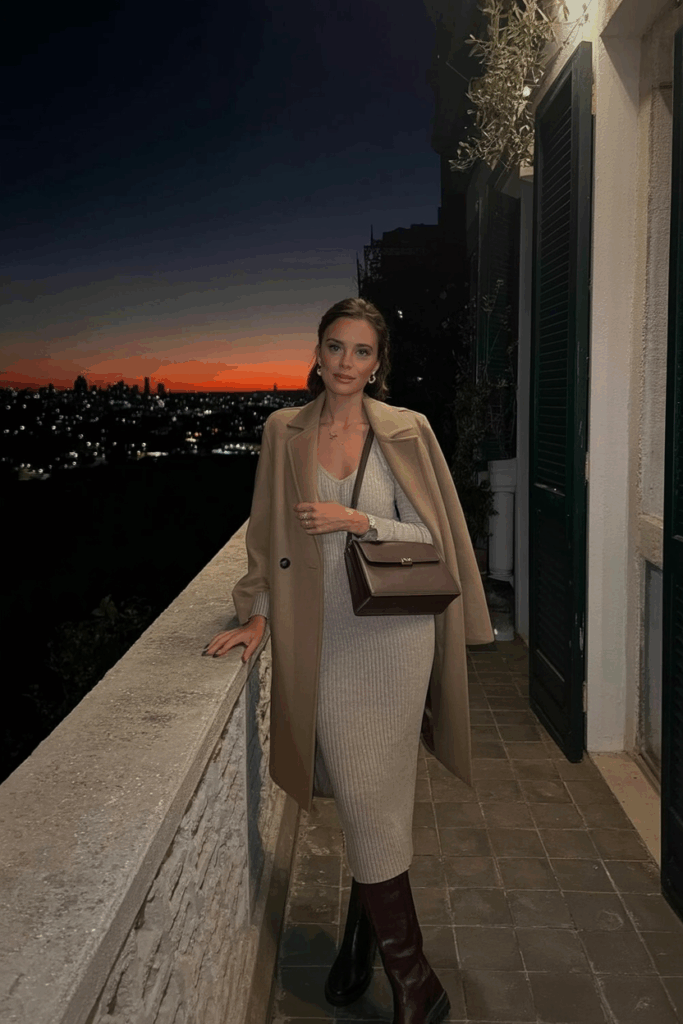 woman wearing a camel wool coat over a fitted knit midi dress, tall brown boots, and a leather shoulder bag