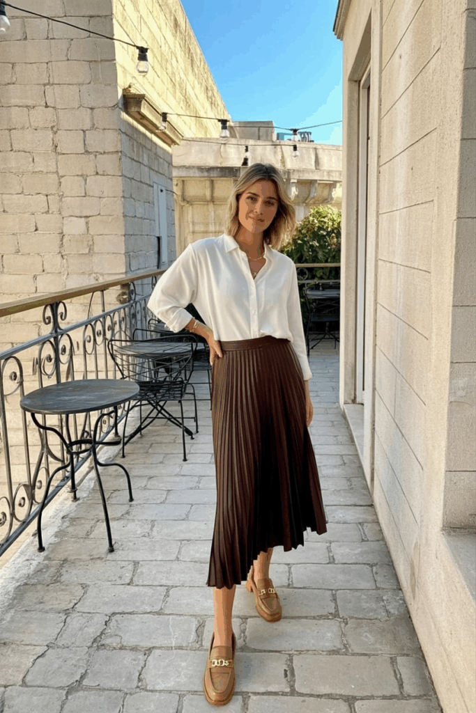 woman wearing a white blouse tucked into a brown pleated skirt with tan loafers